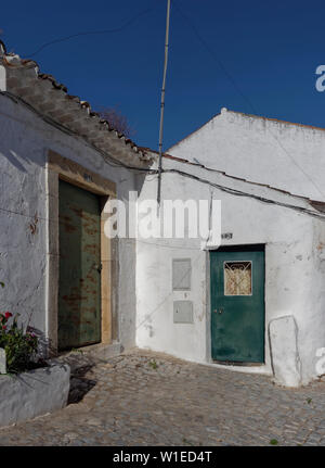 Due sbiadito e ruggine piccole porte in proprietà dipinto di bianco in un piccolo angolo di strada in Estoi, vicino al palazzo. Estoi, Algarve, Portogallo. Foto Stock