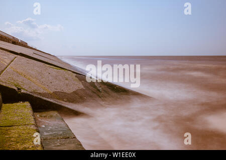 Una lunga esposizione dell'acqua di mare e le onde di colpire una pendenza revetment in calcestruzzo o seawall come parte del litorale le misure di difesa contro le inondazioni Foto Stock