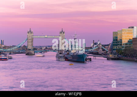 Il Tower Bridge con HMS Belfast al tramonto con il cielo viola sopra il fiume Thames, London, England, Regno Unito, Europa Foto Stock