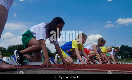 Le ragazze preparano ai blocchi di partenza ad una pista di atletica in bright sole estivo Foto Stock