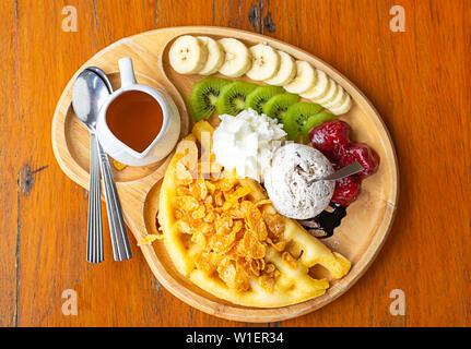 Acqua dolce versare la cialda con gelato e frutta incluse le banane, kiwi e fragole in piatto di legno sul tavolo. Foto Stock