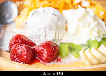 Acqua dolce versare sui frutti incluse le banane, kiwi e fragole con gelato nel piatto di legno sul tavolo. Foto Stock