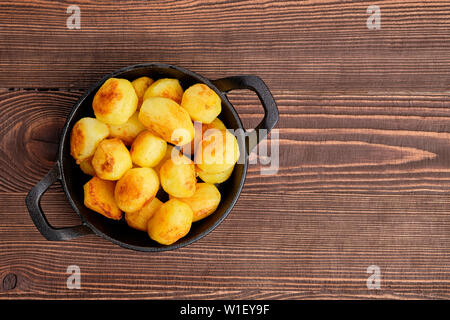 Patate cotte in padella in ghisa sul naturale sfondo di legno Foto Stock