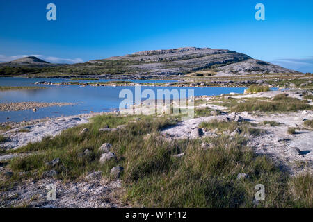 Una lunga esposizione della stupefacente e Marte come il paesaggio che è il Burren National Park, County Clare, Irlanda al tramonto con il piccolo lago nel foregro Foto Stock
