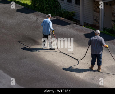 Lavoratori la spruzzatura di asfalto o sigillante di asfalto sulla carreggiata Foto Stock