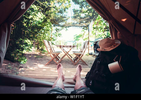 Vista delle gambe di un escursionista uomo appoggiato a piedi nudi in una tenda da campeggio, viaggio di scoperta, il concetto di punto di vista shot Foto Stock