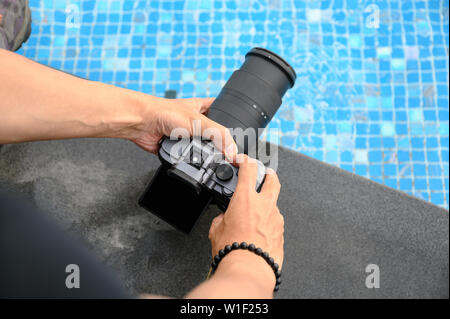 Mano azienda mirrorless fotocamera con zoom per scattare una foto sul bordo della piscina Foto Stock