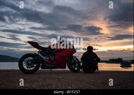 Giovane biker seduto sul lato del grande lo sport bike con escursione al tramonto sul serbatoio Foto Stock