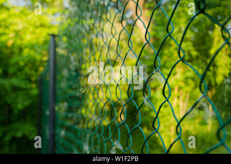 Close up della catena di metallo-link in giardino. Maglie a losanga recinto di filo su sfocato sfondo verde. Reticolo di ferro net in estate patterning. Griglia in sunny