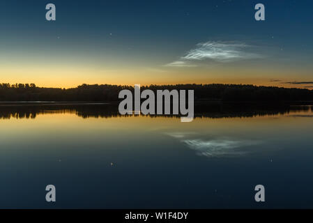 Incredibile paesaggio notturno con argentea luminosa nuvole e stelle nel cielo sopra il lago e i loro riflessi nell'acqua Foto Stock