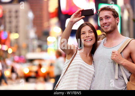 Travel Tourist giovane tenendo selfie con lo smartphone in New York City, Stati Uniti d'America. Self-portrait foto su Times Square di notte. Bella giovani turisti divertendosi, Manhattan STATI UNITI D'AMERICA. Donna asiatica, uomo caucasico Foto Stock