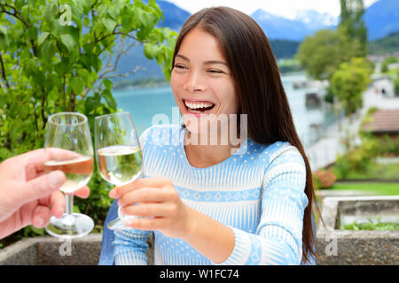 Giovane tostare il bicchiere di vino presso il ristorante all'aperto. Donna asiatica tifo con alcool bere nelle Alpi svizzere, Svizzera in estate in terrazza esterna vicino al lago. Foto Stock