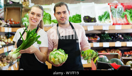 Giovane uomo e donna venditori che mostra il cipollotto e il cavolo nero nel supermercato Foto Stock