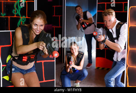 Giovani amici eccitato in canottiere e con pistole laser giocando emotivamente tag laser game in camera Foto Stock