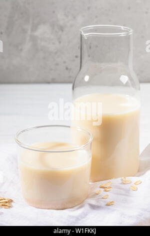 Close-up di vetro senza latte e derivati del latte di avena e fiocchi sul tovagliolo bianco su sfondo di calcestruzzo. Foto Stock