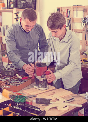 Felice unione falegname uomo e adolescente con asse di legno che lavorano in macchina emerying in officina Foto Stock