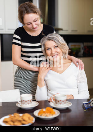 Ritratto di positivo donna matura e ragazza di adulti che abbraccia calorosamente in cucina Foto Stock