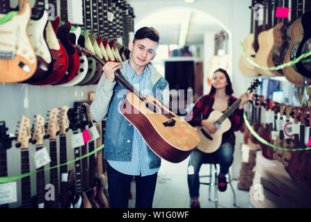 Maschi e femmine di adolescenti scegliendo chitarre acustiche in guitar shop Foto Stock