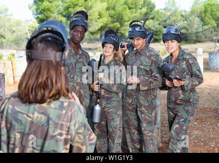 Quattro diligente allegro positivo principianti attento ascolto istruzioni sulla pistola del marcatore prima di paintball partita da allenatore femmina Foto Stock