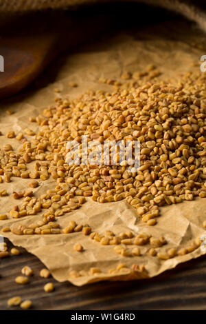 Secchi, materie fenugreek seme su marrone carta da imballo su tavola in legno rustico sfondo con il fuoco selettivo Foto Stock