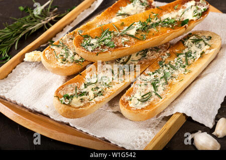 Baguette affettata tostare il pane con burro e aglio ed erbe su un vassoio e scuro dello sfondo. Primo piano Foto Stock