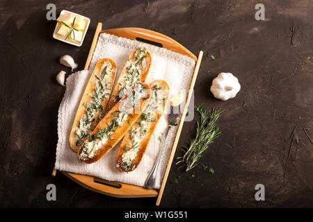 Baguette affettata tostare il pane con burro e aglio ed erbe su un vassoio e scuro dello sfondo. Vista da sopra con copia spazio. Foto Stock