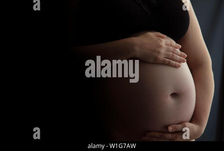 Donna incinta tenendo un baby urtare contro uno sfondo scuro Foto Stock