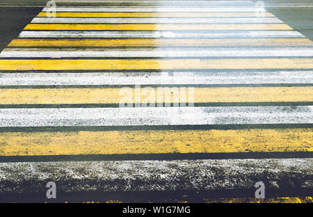 Strada sdrucciolevole con un attraversamento pedonale dipinte in giallo e bianco Zebra con abbagliamento dopo la pioggia. Foto Stock