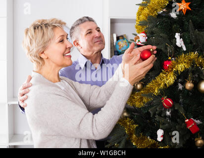 L uomo e la donna 52-56 anni sono riagganciare Nuovo Anno di giocattoli su un abete bianco prima di Natale. Foto Stock