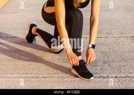 Closeup Ritratto di giovane attraente sportivo da donna in nero sporwear in mattinata sulla strada in piedi sul ginocchio e la preparazione per la formazione, la legatura lacci delle scarpe Foto Stock