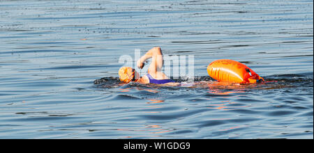 Veiw laterale di una donna che si allontana dalla telecamera in un arancione cuffia da bagno con un arancione di sicurezza dispositivo di galleggiamento srapped per la sua vita. Foto Stock