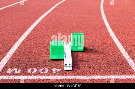 Una serie di blocchi di colore verde sono pronti per essere utilizzati in una gara impostato su a 400 metri la linea di partenza su una pista rossa. Foto Stock