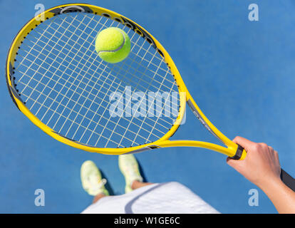 Tennis giocatore in possesso palla gialla sulla griglia della racchetta. Sport atleta femminile prendendo a piedi selfie mostrando le scarpe running su blu hard court. POV closeup di apparecchiature, neon yellow calzature alla moda. Foto Stock