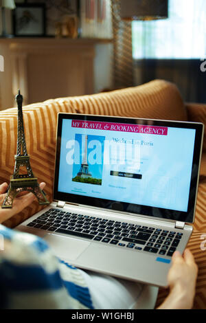 La casalinga moderna con la torre Eiffel souvenir hotel prenotazione online sul sito web di viaggio comodamente seduti sul divano di casa moderna nella soleggiata caldo giorno d'estate. Foto Stock