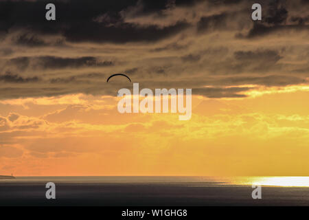 Parapendio battenti alto sopra l'oceano al tramonto di un giorno nuvoloso Foto Stock