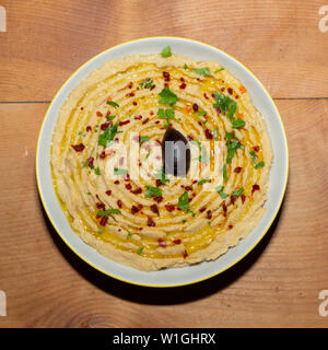 Hummus - Oriental antipasto - pasta di ceci in una ciotola su una tavola di legno, guarnite con prezzemolo, pepe, olio d'oliva Foto Stock