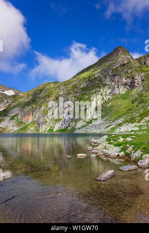 Gregge di piccoli pesci, ripple nel pulire, acque trasparenti del famoso lago di rene, uno dei sette laghi di Rila, epica, soleggiato cime rocciose ed un cielo blu Foto Stock