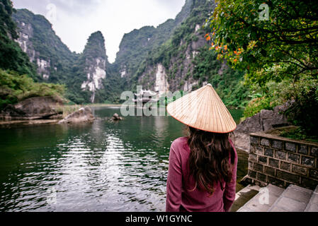 Ragazza vietnamita con il cappello di paglia di Trang un paesaggio panoramico formato da torri carsiche e piante lungo il fiume (Patrimonio Mondiale dell'UNESCO). Si tratta di halon Foto Stock