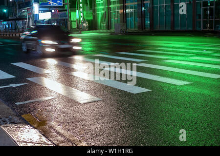 Seoul, Corea del Sud - 30.10.18: auto passa rapidamente durante la notte su un attraversamento pedonale. attraversamento pedonale di notte di luce verde. sentieri sul bagnato Foto Stock