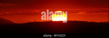 Sole rosso al tramonto sotto le nuvole sopra l'orizzonte. Epic quadro drammatico del cielo. Foto Stock