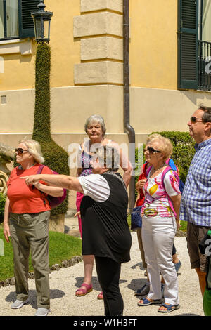 LENNO, LAGO DI COMO, Italia - Giugno 2019: Tour guida sottolineando qualcosa di interesse per un gruppo di visitatori nel parco della Villa del Balbianello a L Foto Stock