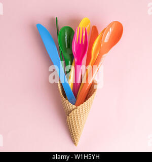 Piatto di laici colorato con posate di plastica nel cono gelato contro rosa pastello background creativo minimo il cibo e le bevande del concetto. Foto Stock