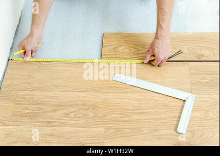Installazione di un tavolato di laminato. Lavoratore con le mani in mano sono la misurazione della distanza dalla parete. Foto Stock