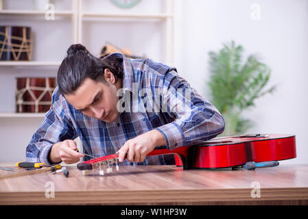 Giovane bello repairman riparazione di chitarra Foto Stock