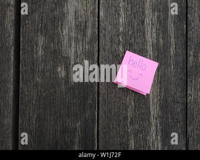 Ciao testo lettera su sfondo di legno. Vista superiore rosa nota di Promemoria ciao con icona Smiley face isolati su grunge di legno. Scrittura di parole con sorriso. Foto Stock