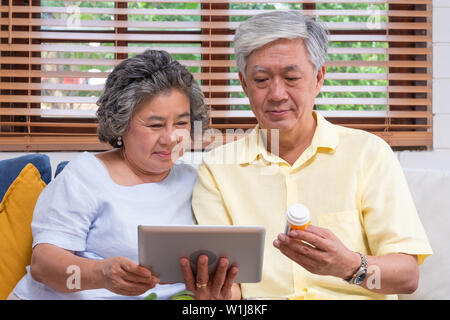 Asian coppia senior utilizzare computer tablet ricerca medico prescrizione pillola seduti sul divano di casa,senior imparare a utilizzare la tecnologia Foto Stock