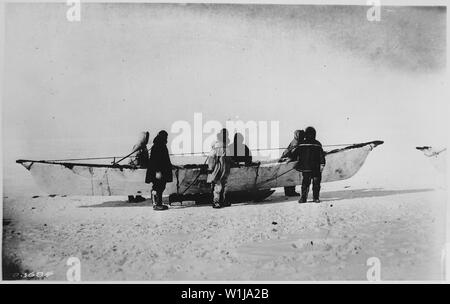 Sei eschimesi in piedi accanto a skinboat nativo (umiak) sulla slitta, punto Barrow, Alaska, 1935 Foto Stock