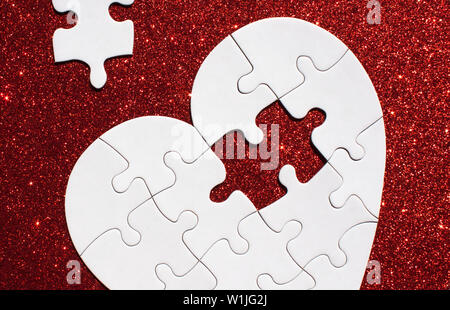 Bianco a forma di cuore puzzle con parte mancante su red sparkle sfondo. Foto Stock