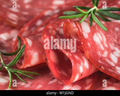 Extreme close up salame tagliato a fette. Materie salsiccia affumicata fette di close-up. Alcuni pezzi o più fette. Vista laterale di materie smocked le fette di salsiccia con foglie di rosmarino Foto Stock