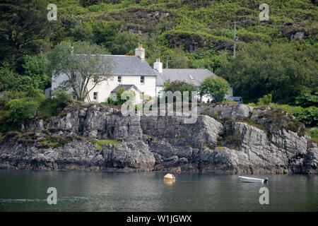 Croft casa sul bordo d'acqua del Loch in Scozia. Una barca è ormeggiata vicino al litorale roccioso. Foto Stock
